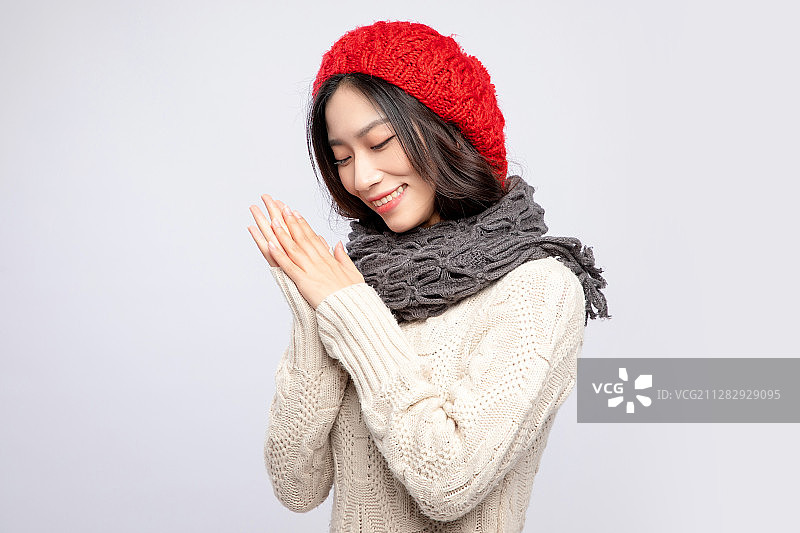 灰色背景里，身穿米色毛衣的带着红色绒线帽的美丽亚洲女孩图片素材