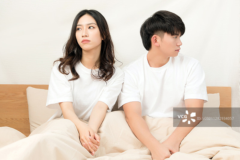 穿着白色短袖坐在床上的正在吵架的一对亚洲年轻情侣图片素材
