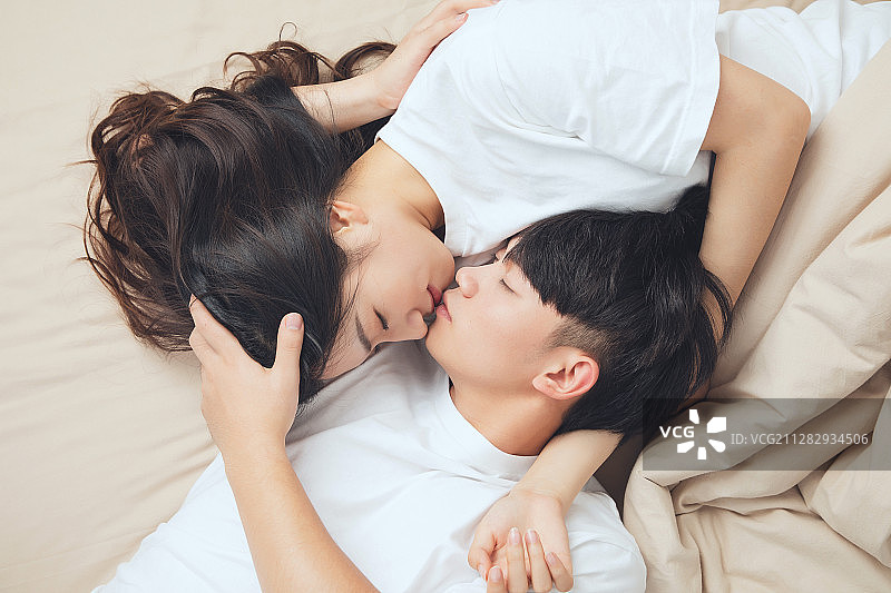 一对亚洲年轻情侣躺在床上，互相看着对方，非常亲密的样子图片素材