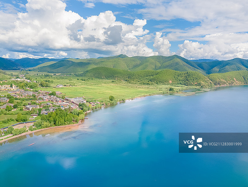 航拍天气晴朗蓝天白云的泸沽湖以及周边建筑和远山图片素材