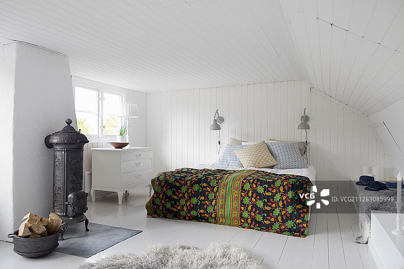 卧室里带铸铁炉的床上铺着彩色床罩图片素材