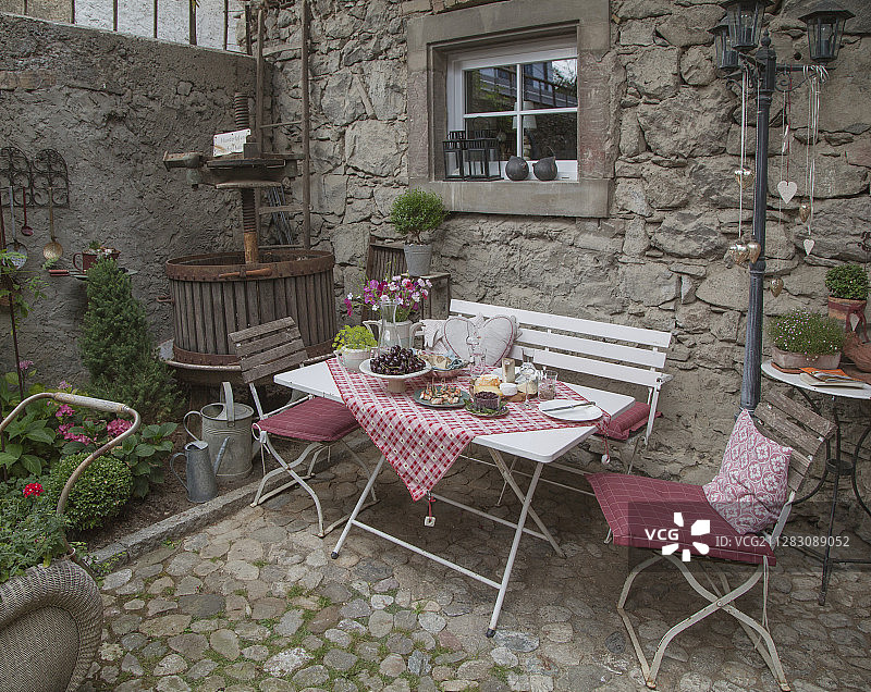 鹅卵石露台上葡萄酒压榨机旁的餐桌、椅子和长凳图片素材