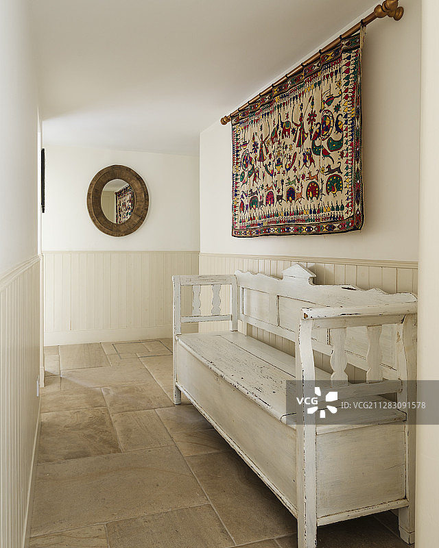 走廊中白色木凳上方的部落风挂毯图片素材
