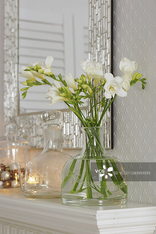 壁炉架上老式玻璃瓶中的白色小苍兰图片素材