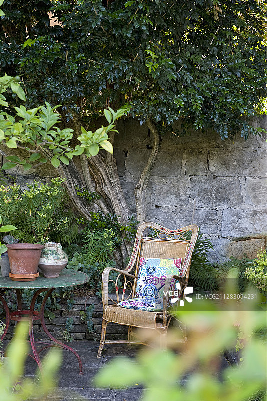 地中海花园中靠在石墙上的藤制扶手椅图片素材