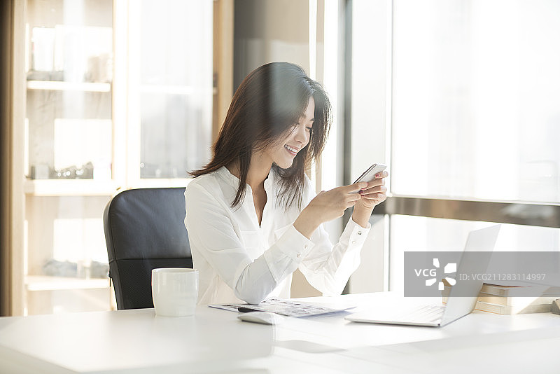 年轻商务女士在办公室使用智能手机图片素材