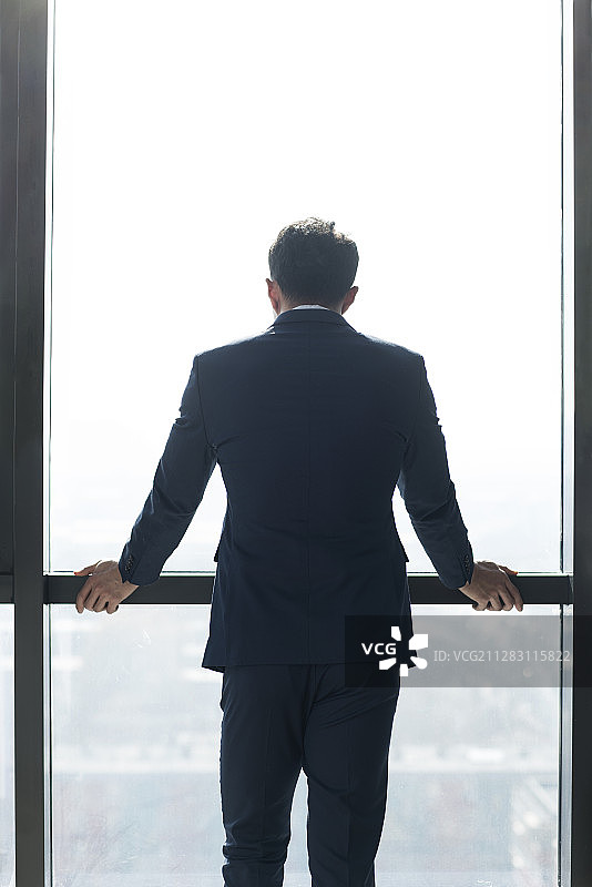 年轻商务男子站在窗前看向窗外图片素材