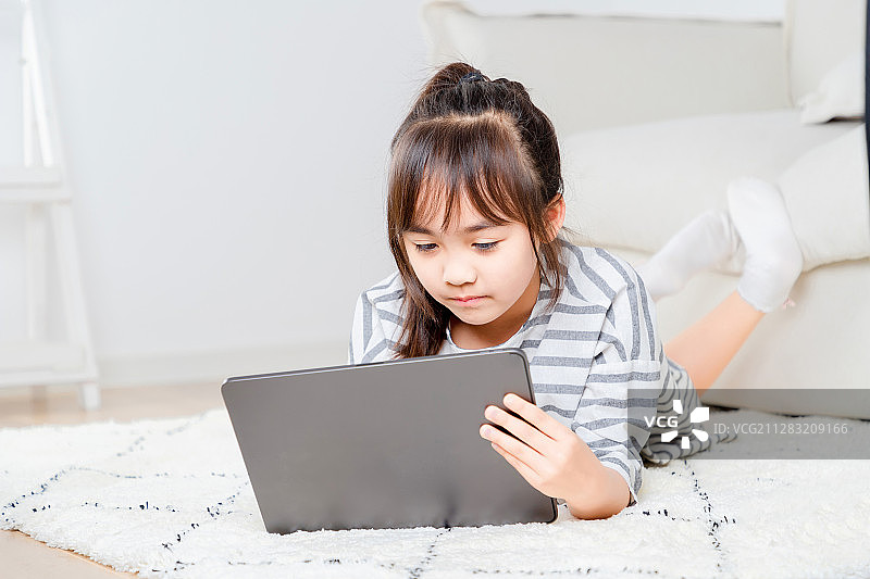 趴在地毯上玩平板电脑的亚洲小女孩图片素材
