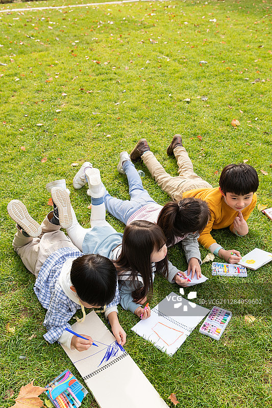 可爱的小朋友们趴草地上画画图片素材