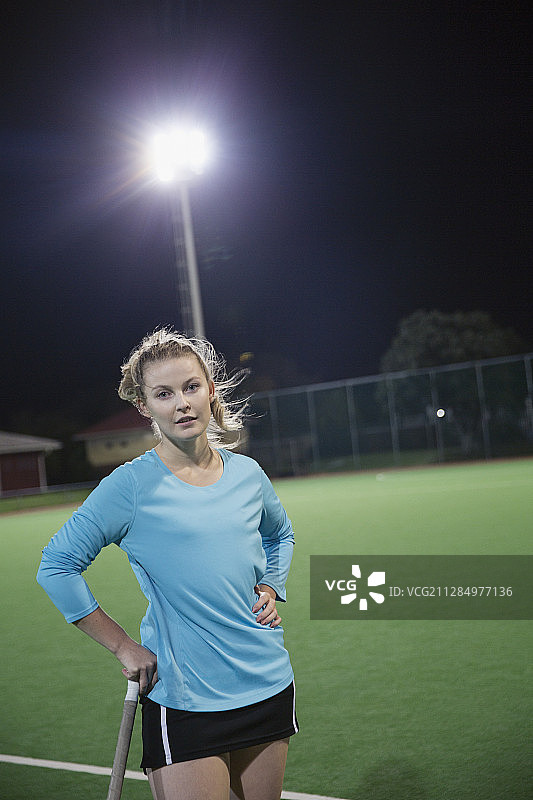 夜晚球场上表情严肃的年轻女子曲棍球运动员肖像图片素材