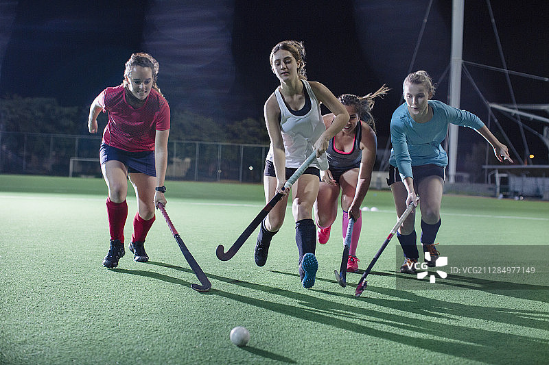 年轻女子曲棍球运动员在夜间球场上奔跑争球图片素材