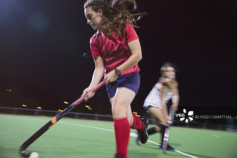 夜间，年轻女子在球场上击球，进行曲棍球运动图片素材