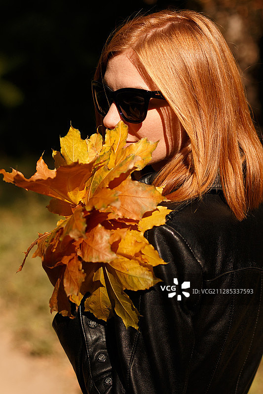 戴着太阳镜的红发年轻女子手持秋叶，乌克兰赫尔松图片素材
