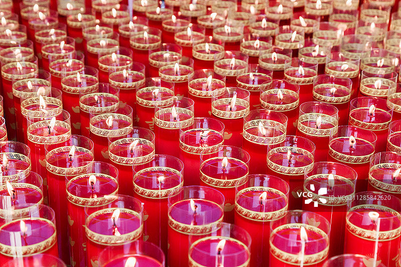 佛教节日中寺庙里点燃一片整齐排列红色圆柱形祈福酥油灯图片素材