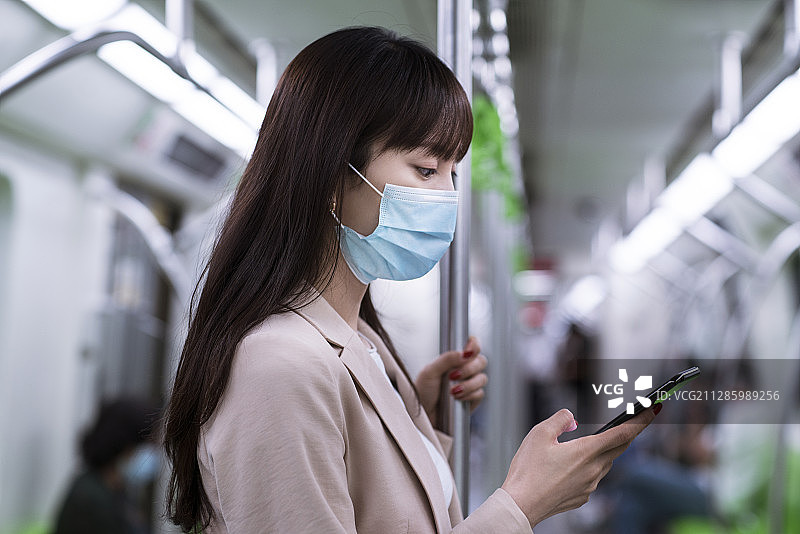 年轻女子戴着防护口罩在地铁上使用智能手机图片素材