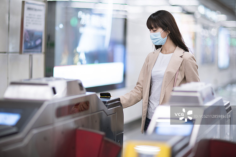 年轻女子戴着口罩使用智能手机扫码出地铁站图片素材