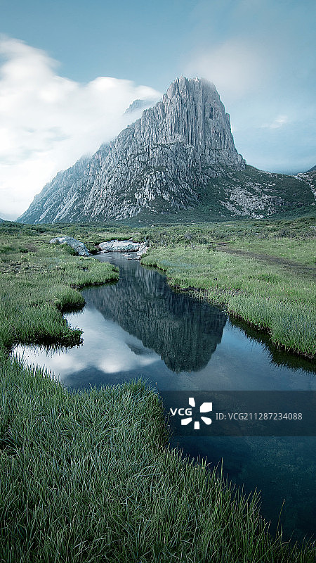 云雾缠绕在山间，绿色的草甸上有一条溪流图片素材
