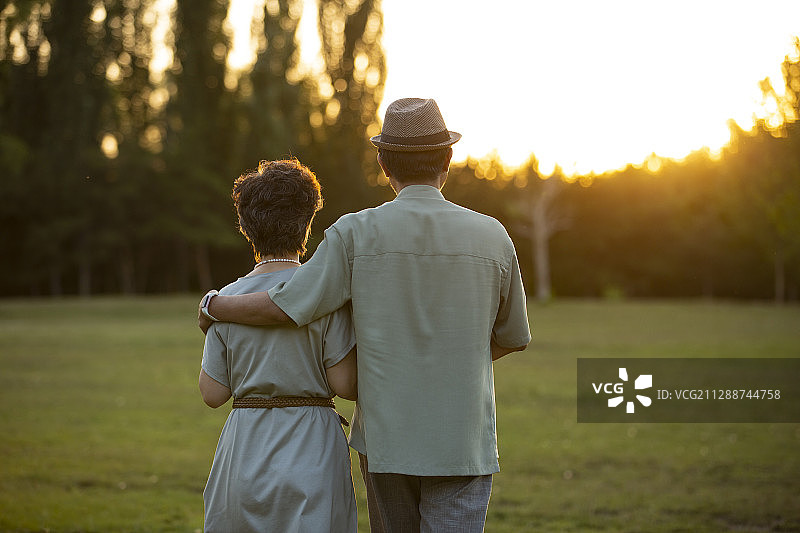 夕阳下老年夫妻在户外公园草地散步图片素材