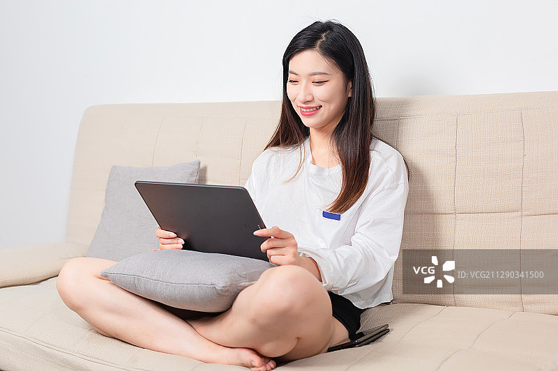 坐在沙发上的美女，正在使用平板电脑图片素材