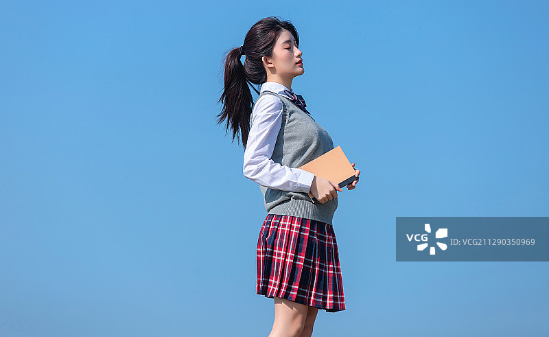 蓝色天空背景下,拿着书本的亚洲女学生图片素材