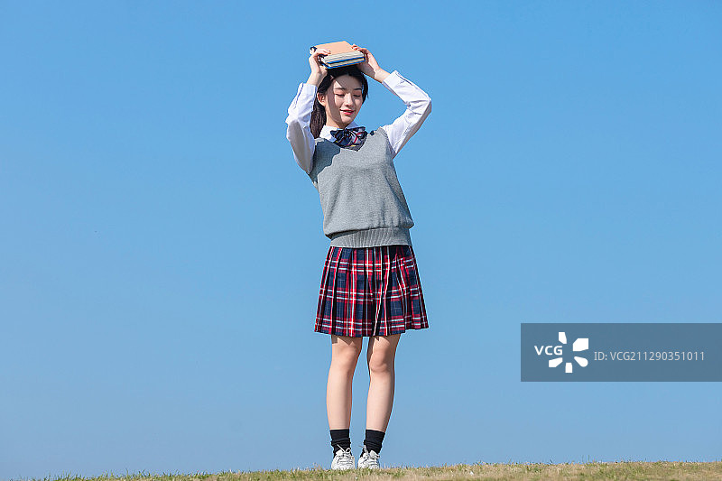 蓝色天空背景下,拿着书本的亚洲女学生图片素材