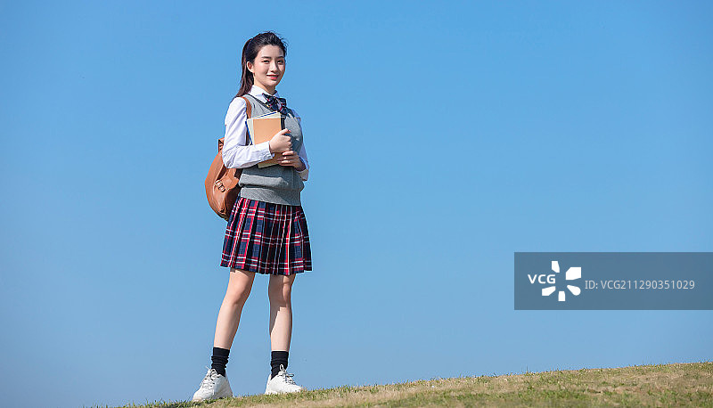 蓝色天空背景下,拿着书本的亚洲女学生图片素材