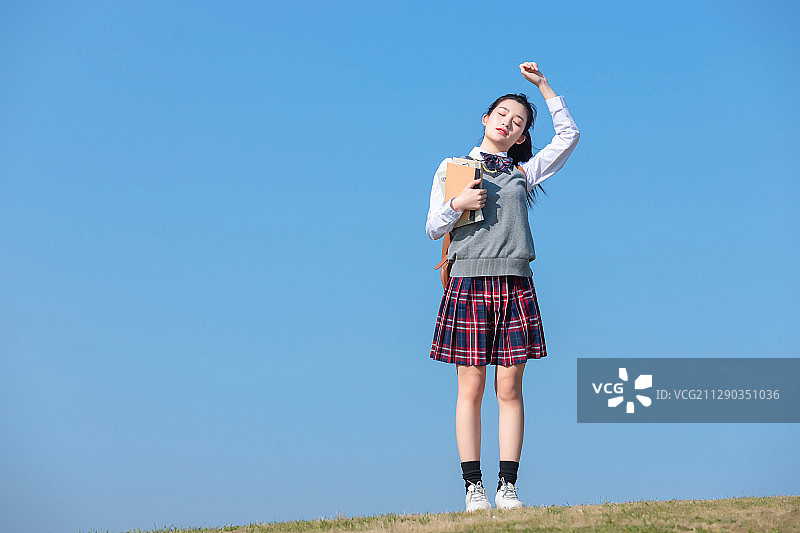 蓝色天空背景下,拿着书本的亚洲女学生图片素材