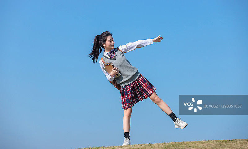 蓝色天空背景下,拿着书本的亚洲女学生图片素材