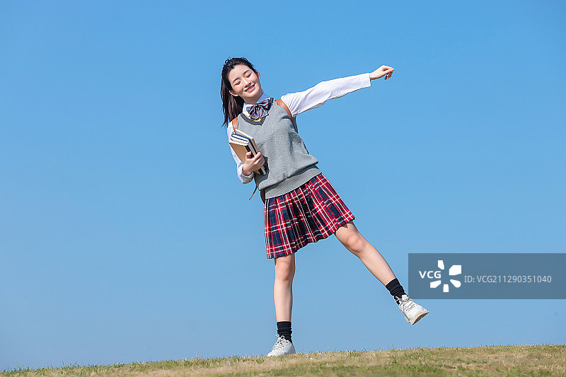 蓝色天空背景下,拿着书本的亚洲女学生图片素材