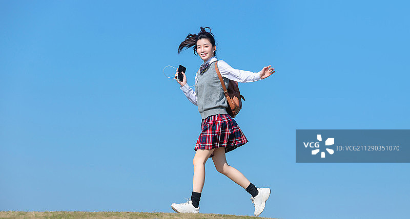 蓝色天空背景下，正在慢跑的亚洲女学生图片素材