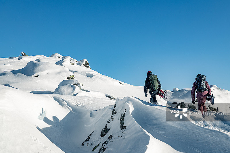 在奥地利山脉徒步前往山顶的单板滑雪者图片素材