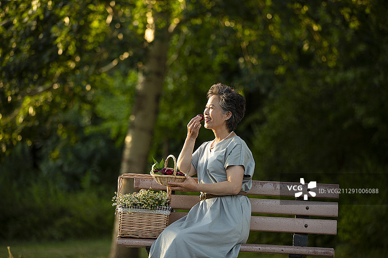 老年女人坐在公园长椅上挑选野餐篮子里的水果图片素材