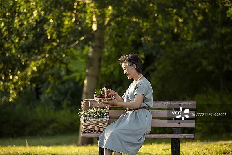 老年女人坐在公园长椅上挑选野餐篮子里的水果图片素材