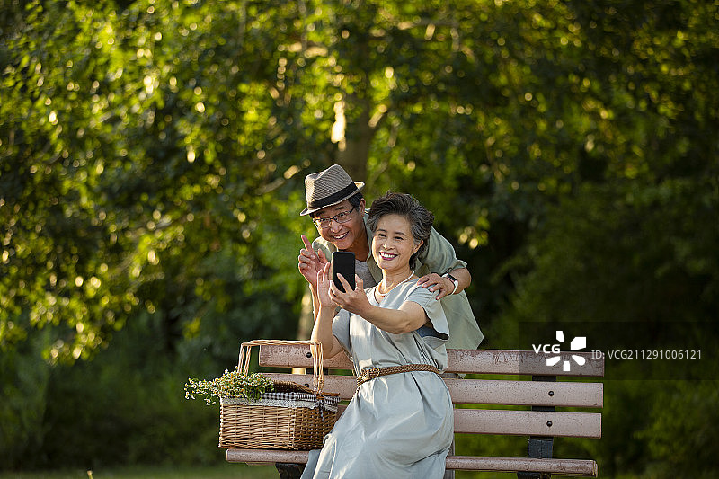 老年夫妻在户外公园的椅子上使用手机视频聊天打招呼图片素材