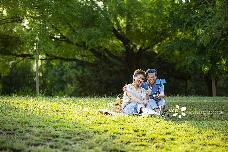老年夫妻在户外公园野餐拿着手机自拍杆视频聊天图片素材