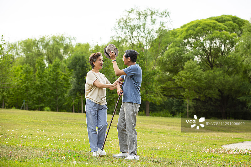老年男人帮助老年女人戴草帽在户外公园散步图片素材