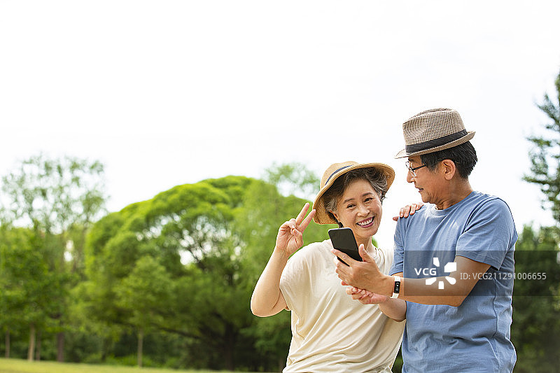 老年夫妻拿着手机自拍在户外公园图片素材