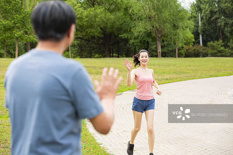 公园跑步青年女子和散步的老年男人打招呼图片素材