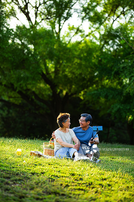 老年夫妻在户外公园野餐拿着手机自拍杆视频聊天图片素材