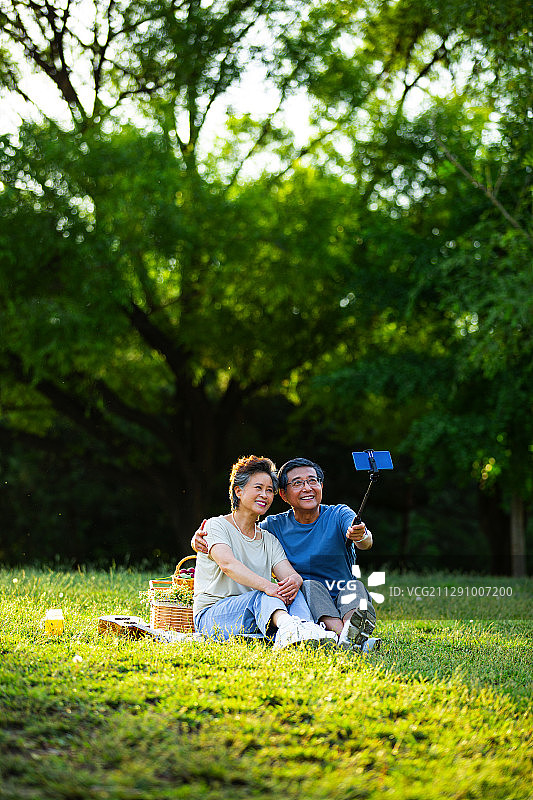 老年夫妻在户外公园野餐拿着手机自拍杆视频聊天图片素材