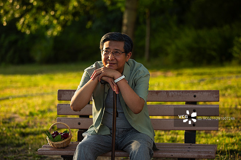 老年男人坐在户外公园长椅上拿着拐棍休息肖像图片素材