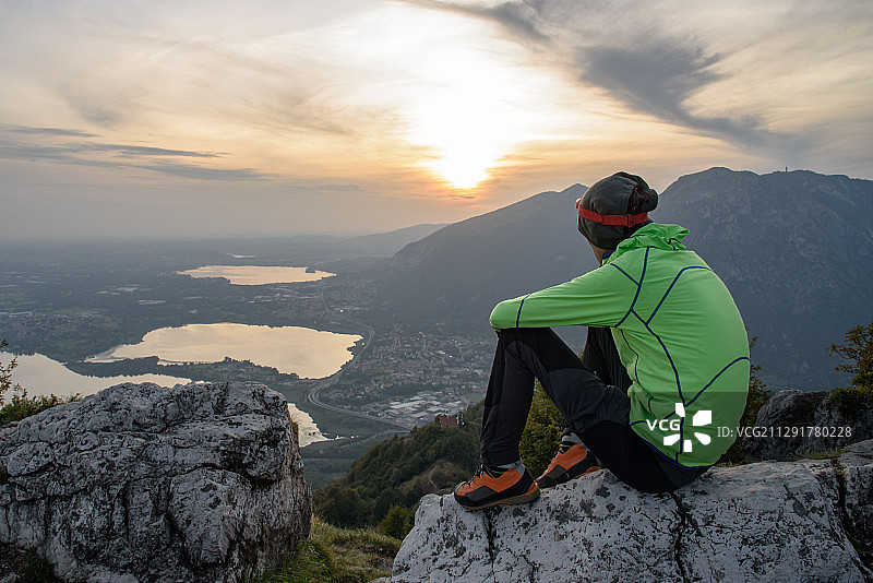 男人坐在意大利莱科加尔比亚泰的岩石上向前看图片素材