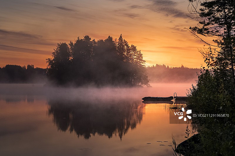 日出时分雾气蒙蒙的湖面映衬着绚丽的橙色天空图片素材