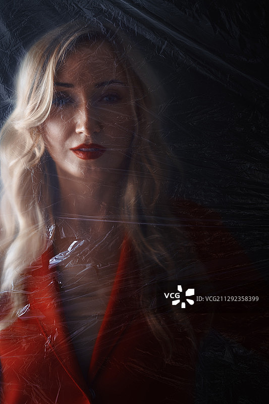 被困在塑料片后面的穿红色外套的金发女人图片素材