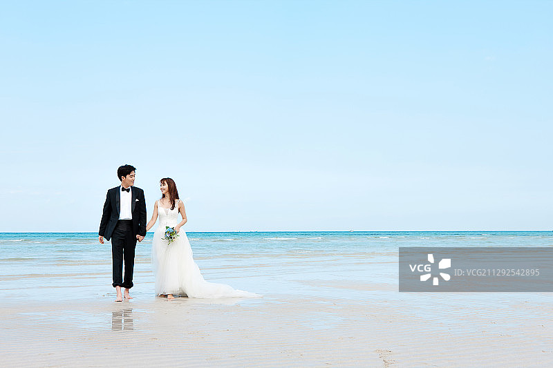 新娘牵着新郎的手在海滩上行走图片素材