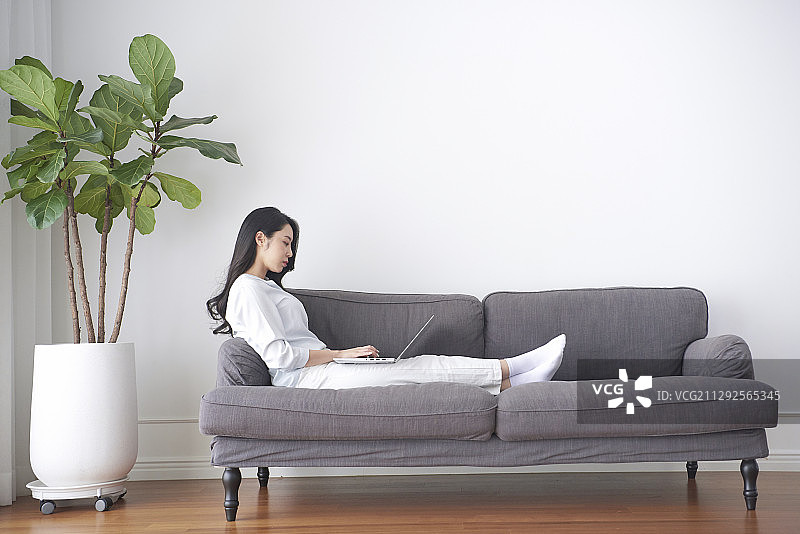 坐在沙发上双腿伸直在家用笔记本电脑工作的女人照片图片素材
