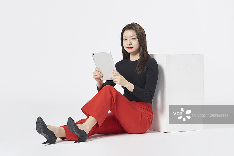 女人坐在椅子上，看着数位平板的影棚照图片素材