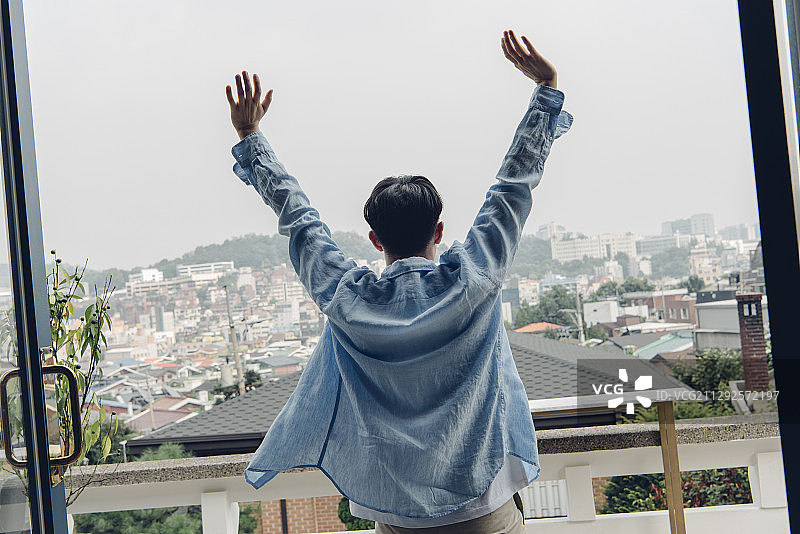 男人早上在阳台上伸展双臂的照片图片素材