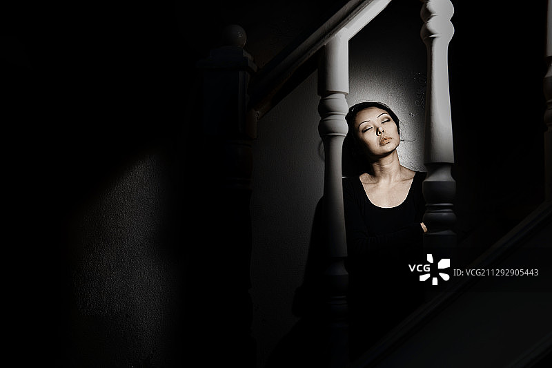 优雅女士闭眼坐在黑暗房间楼梯上图片素材