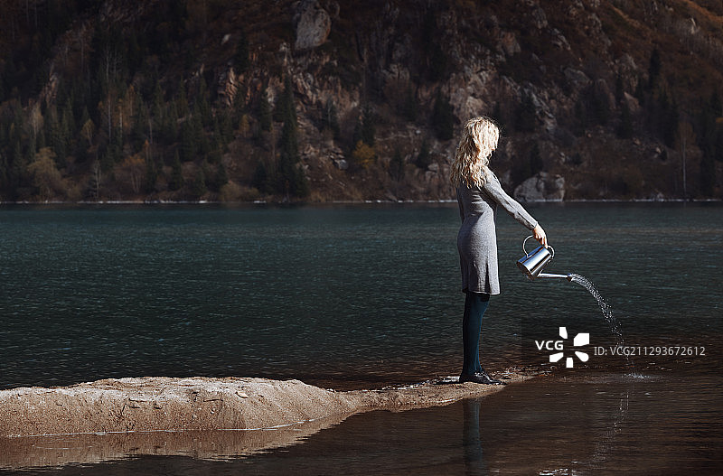 拿着水壶在湖边浇水的妇女，适合做书籍封面图片素材